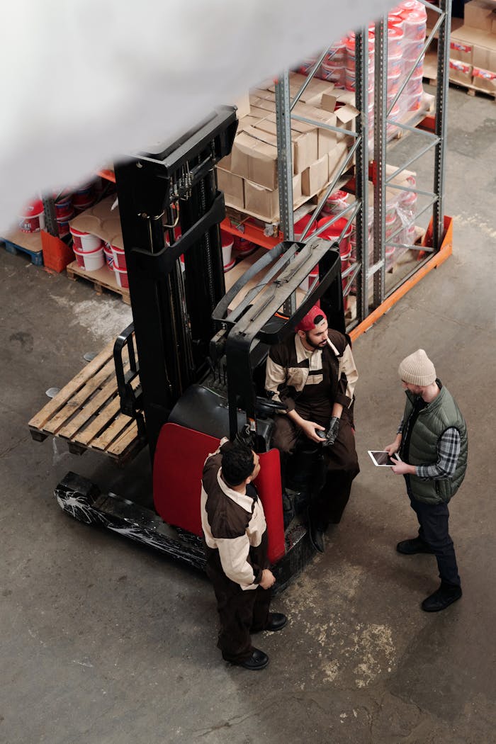 gallery-6 Overhead view of warehouse workers having a meeting with forklift equipment. Collaborative workplace scenario.