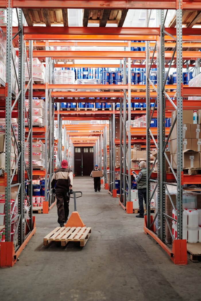hero-img-02 Workers arrange inventory on shelves in a large industrial warehouse.