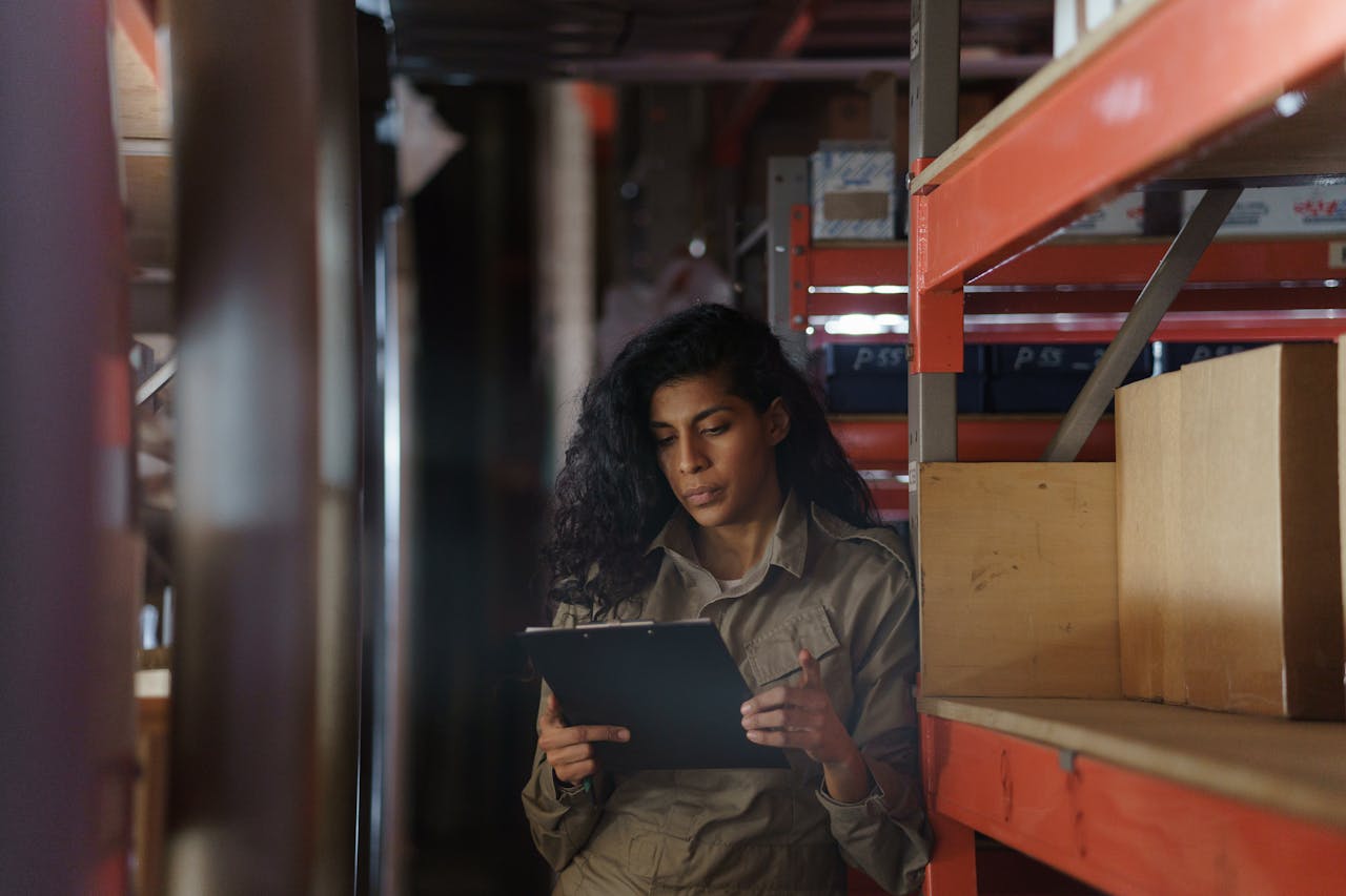 services-03 Woman in warehouse taking inventory with clipboard, focused and pensive.